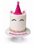 Unicorn themed birthday cake with party hat, sprinkles and minimal white finish on white cake stand