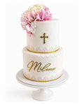 Two-tier ivory fondant cake with blush and white sugar flowers, gold cross detail, lace accents, and personalised gold script on a white cake stand.