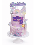 Two-tier roller disco themed cake with pastel colours, disco balls and roller skate decorations finished in white chocolate ganache on white cake stand