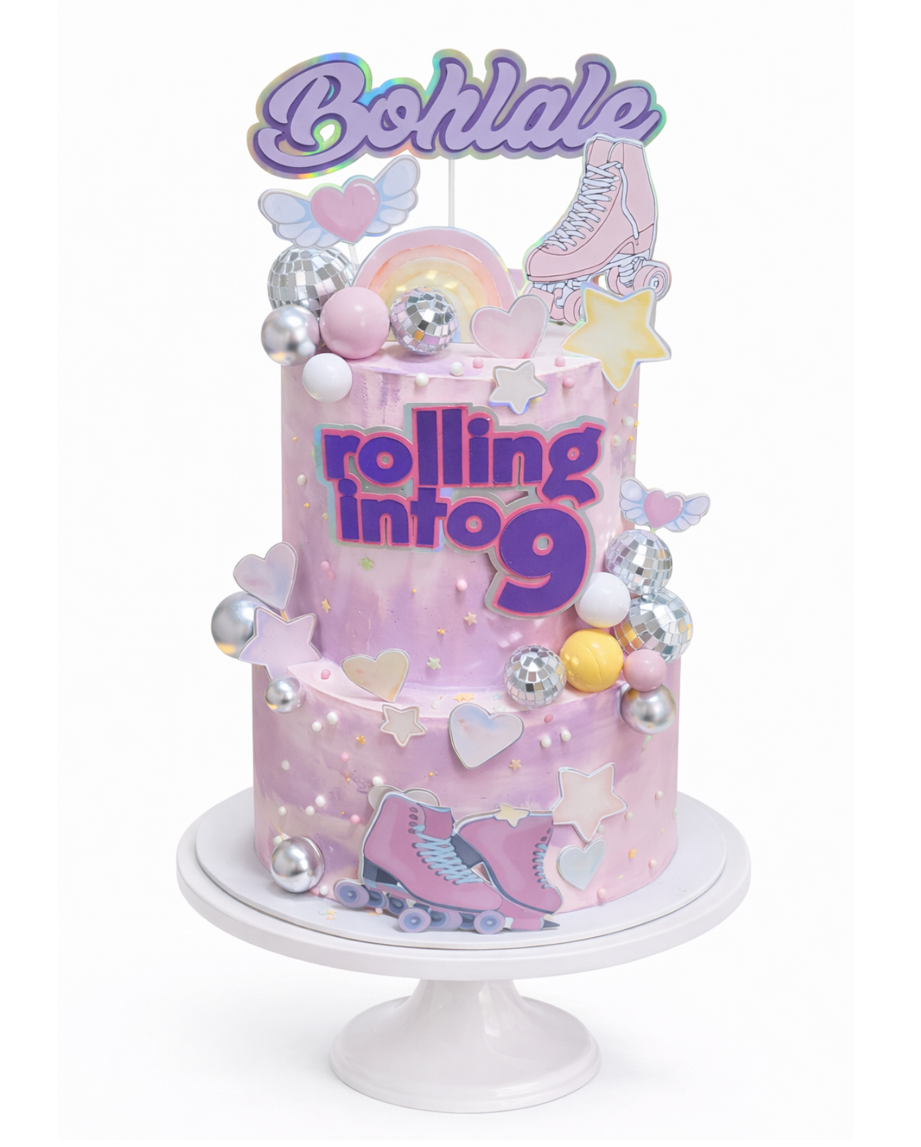 Two-tier roller disco themed cake with pastel colours, disco balls and roller skate decorations finished in white chocolate ganache on white cake stand