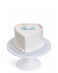 Heart shaped vintage style cake with white chocolate ganache finish and blue “Bride” script on white cake stand